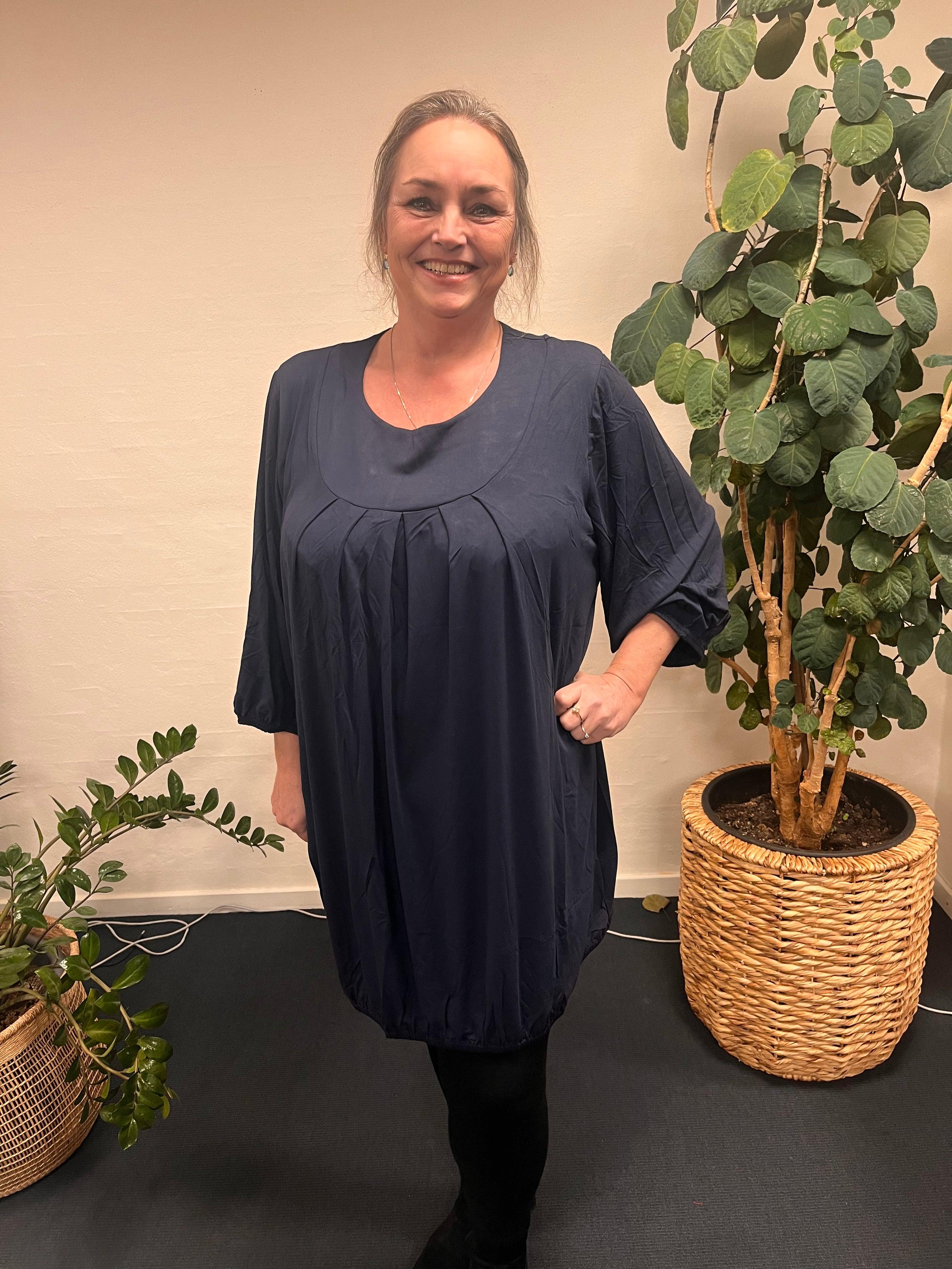 Pronto woman - LisG tunika med flotte læg, stående foran plante.