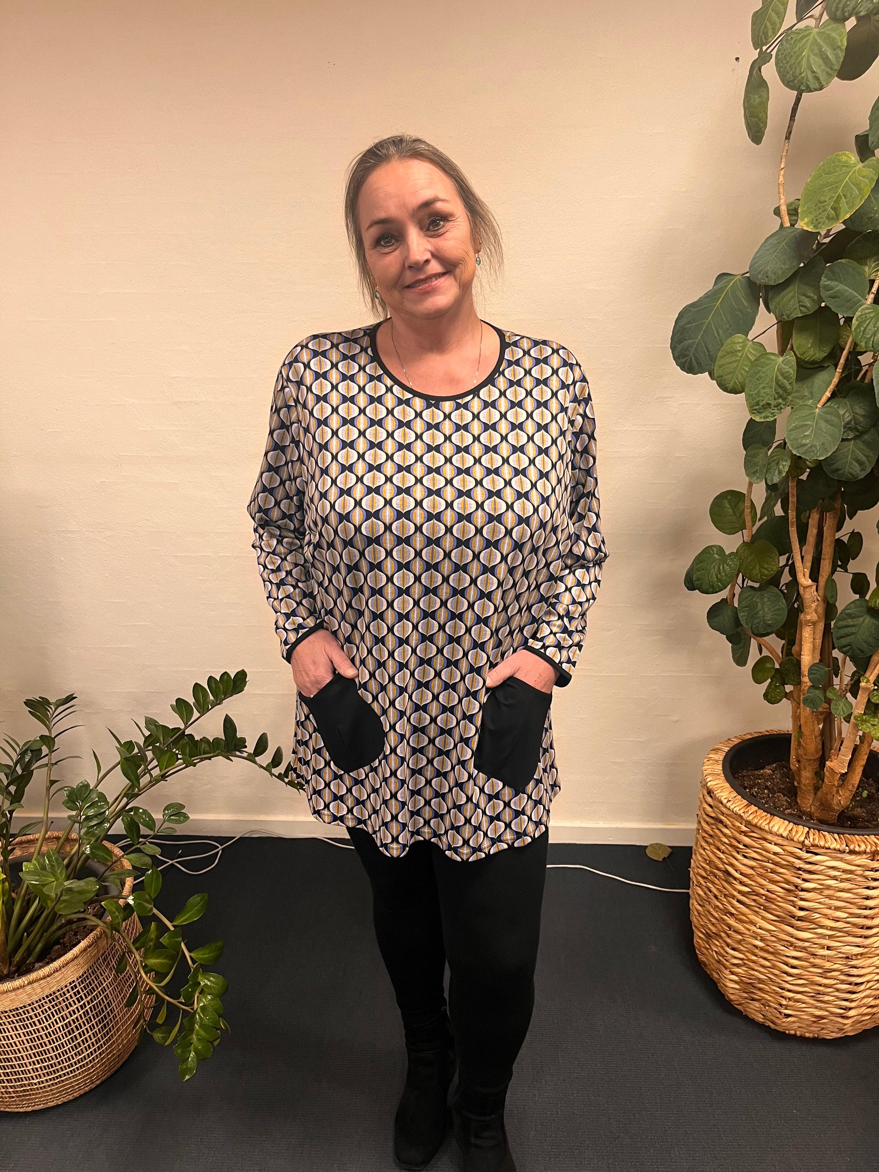 Kvinde iført Pronto Woman - LisG bluse med lommer, står foran plante.