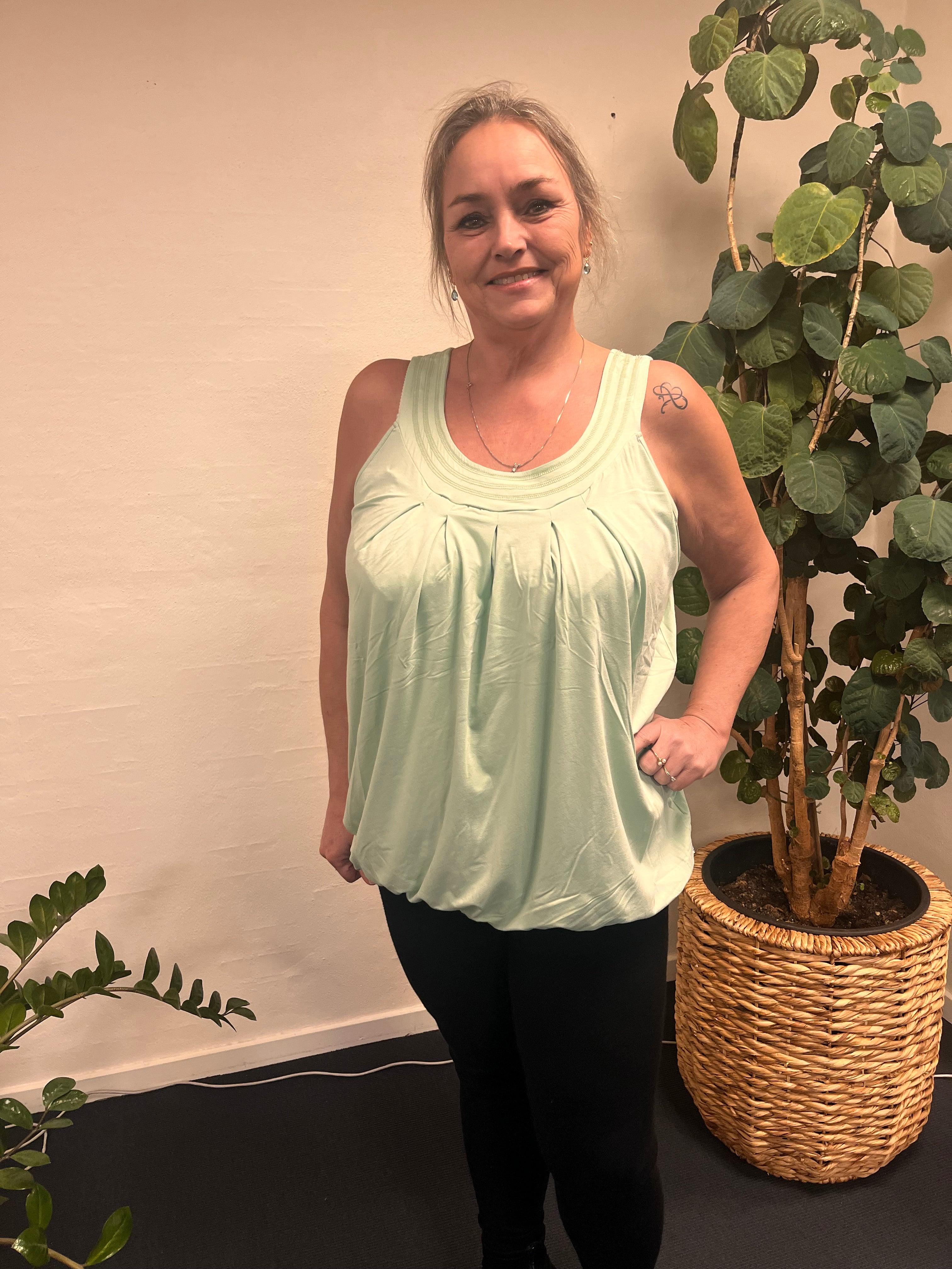 Kvinde iført Zhenzi - LisG æblegrøn top foran plante.