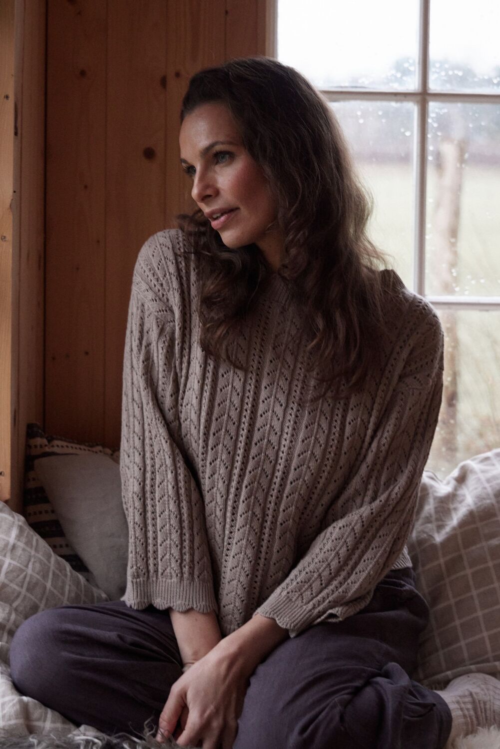 Femme Facon CAROLINE strikbluse, kvinde sidder ved vindue.