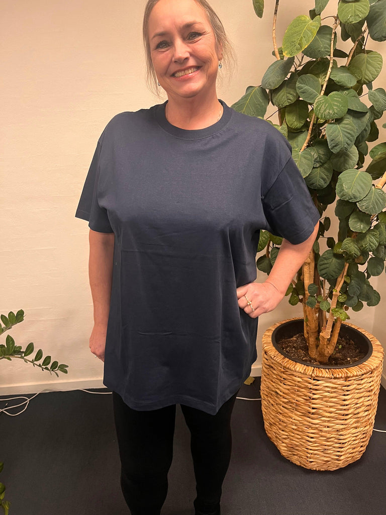 Kvinde i Basic T-Shirt-47, stående foran en plante.