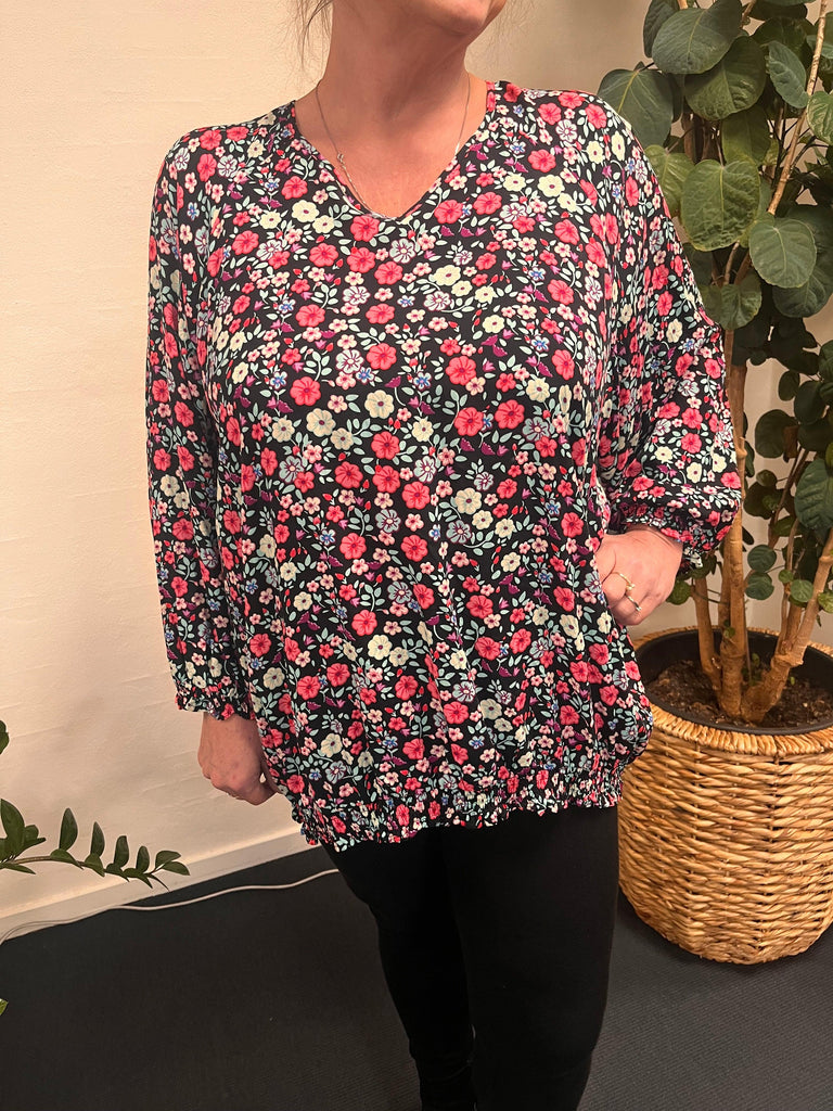 Kvinde iført Studio Augusta blouse-46 foran en plante.